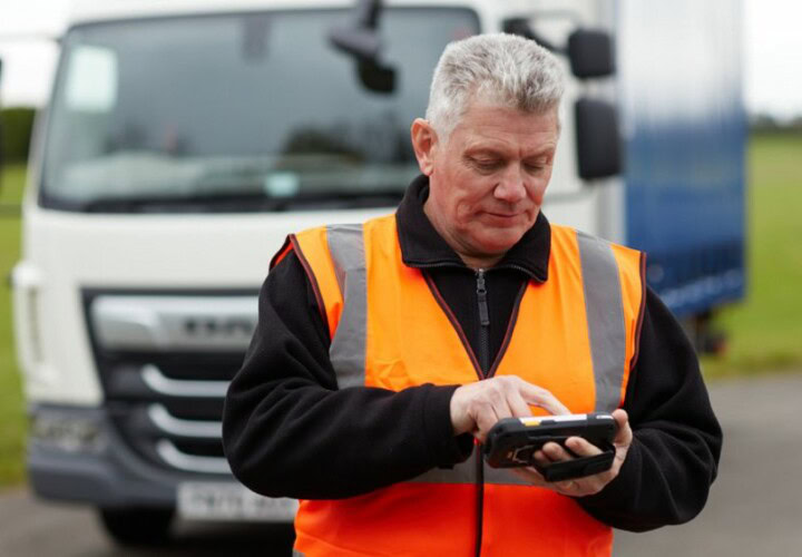 man using microlise tms on a mobile device standing in front of a lorry